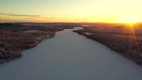 aerial view of sunset over snowy frozen lake in deep forest with hills and mountains