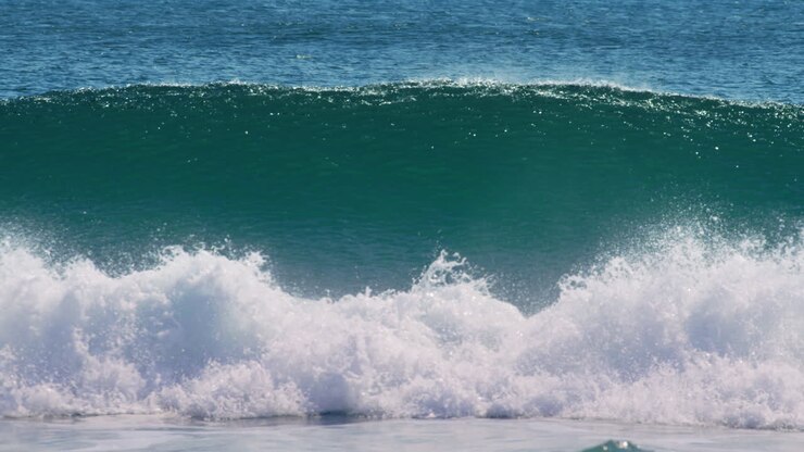 Ocean wave cresting and breaking with white foam under daylight horizon, sparkling glistening mist, slow motion