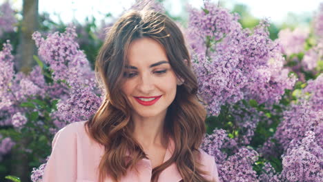 una mujer con una camisa rosa, en un jardín de lilas.