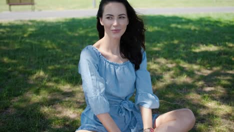 Portrait-of-attractive-brunette-woman-in-blue-dress-sitting-in-a-park