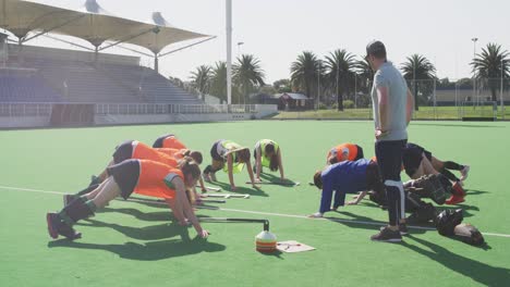 coach watching female hockey players exercising on the field