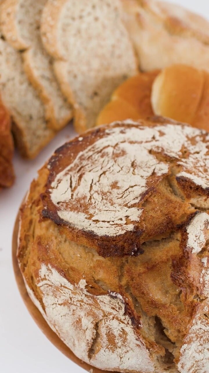 Slow rotation of crusty sourdough loaf on wooden platter against white background with sliced bread.