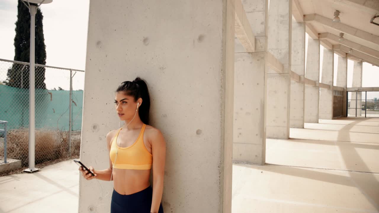 joven deportiva con teléfono inteligente descansando y escuchando música