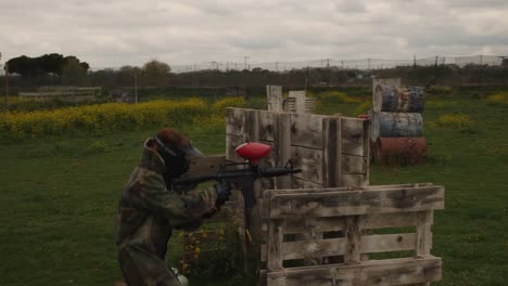 a woman sheltered behind some wooden pallets in a paintball field under a cloudy sky