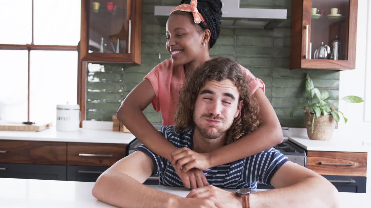 pareja diversa: una joven afroamericana abraza a un joven caucásico en la cocina de una casa