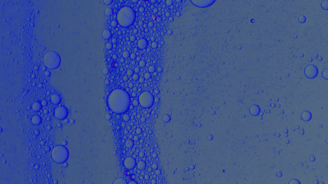 Dirty blue oil flow with black spots slowly with bubbles and dust on surface