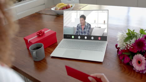 Caucasian-woman-holding-red-envelope-using-laptop-with-biracial-man-on-screen