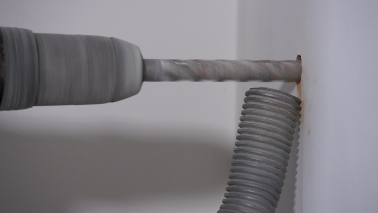 Static shot of maintenance drilling work into a wall with a hoover sucking up the particles