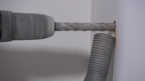 static shot of maintenance drilling work into a wall with a hoover sucking up the particles