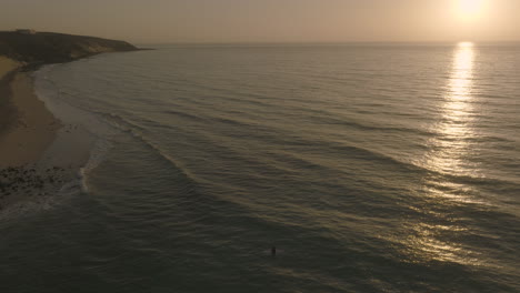 Apple-Prores-422-Surferin-Sitzt-Auf-Einem-Longboard-Und-Beobachtet-Den-Sonnenuntergang-über-Dem-Atlantik-Auf-Den-Kanarischen-Inseln-Von-Fuerteventura-Mit-Küstenstrand,-Gefilmt-Mit-DJI-Mavic-3-Cine