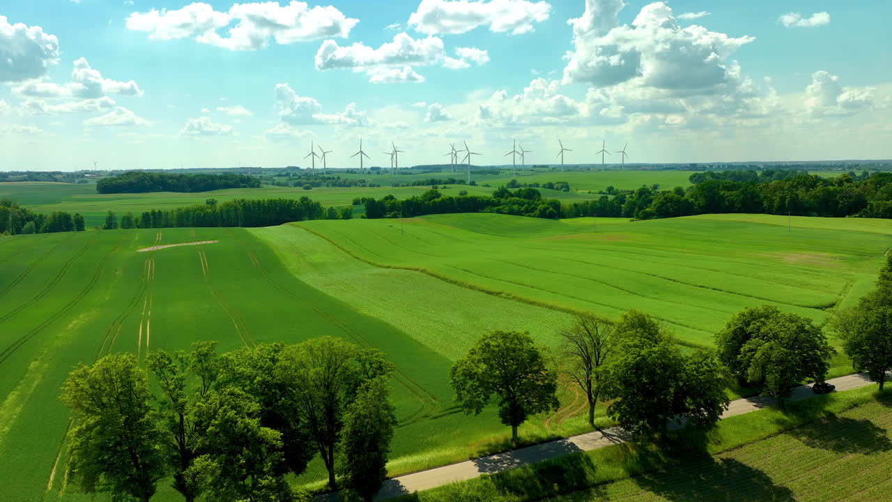 Aerial rural landscape scene features expansive green fields under a bright blue sky with scattered clouds