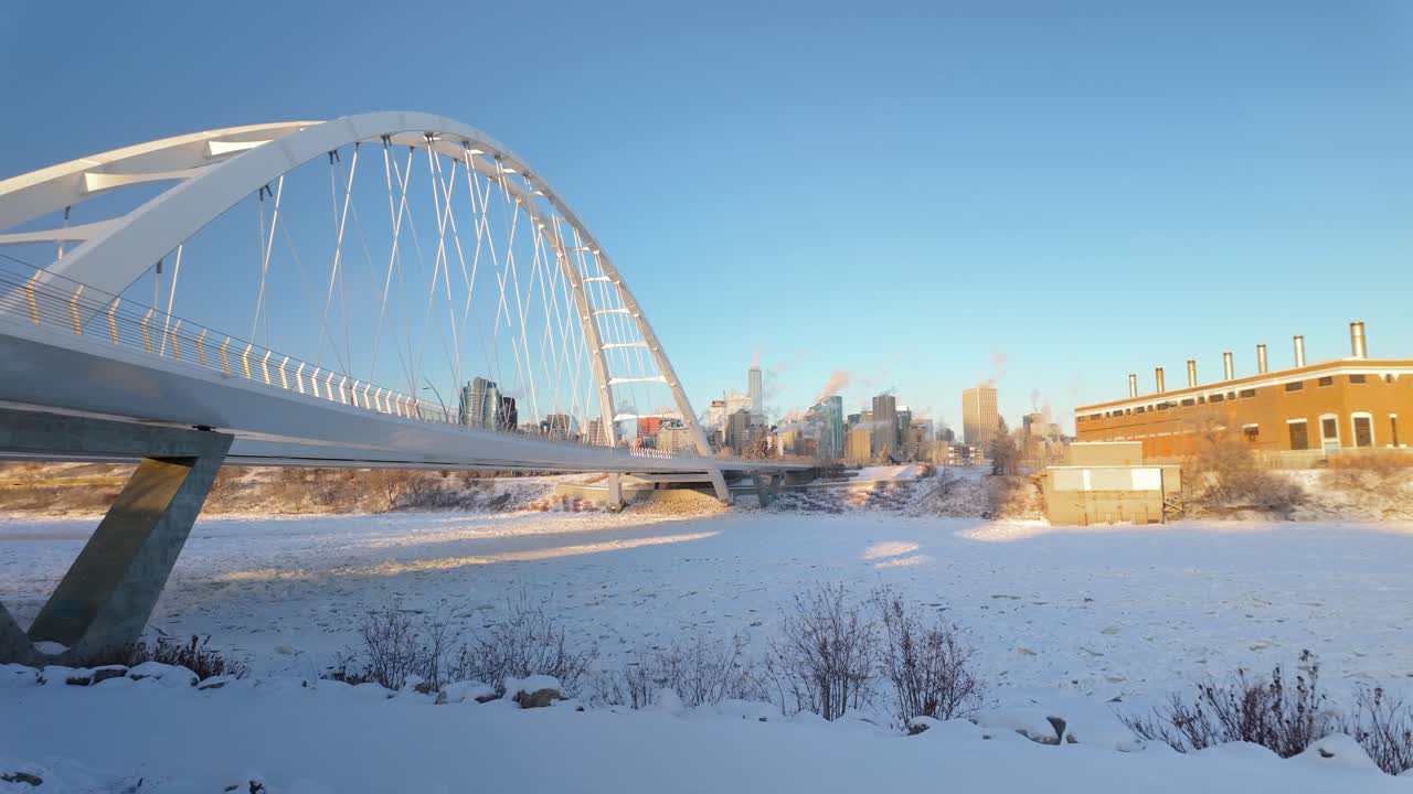 A freezing winter day in Downtown Edmonton, viewed from the Walterdale Bridge, showcasing Highrise buildings, a snowy river valley, and the cold beauty of the city