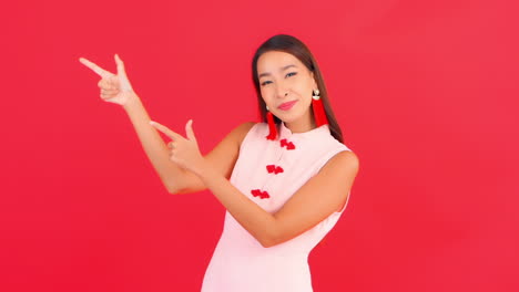 young smiling asian woman pointing left with fingers, isolated on red background for interactive adds, logo or slogan, full frame