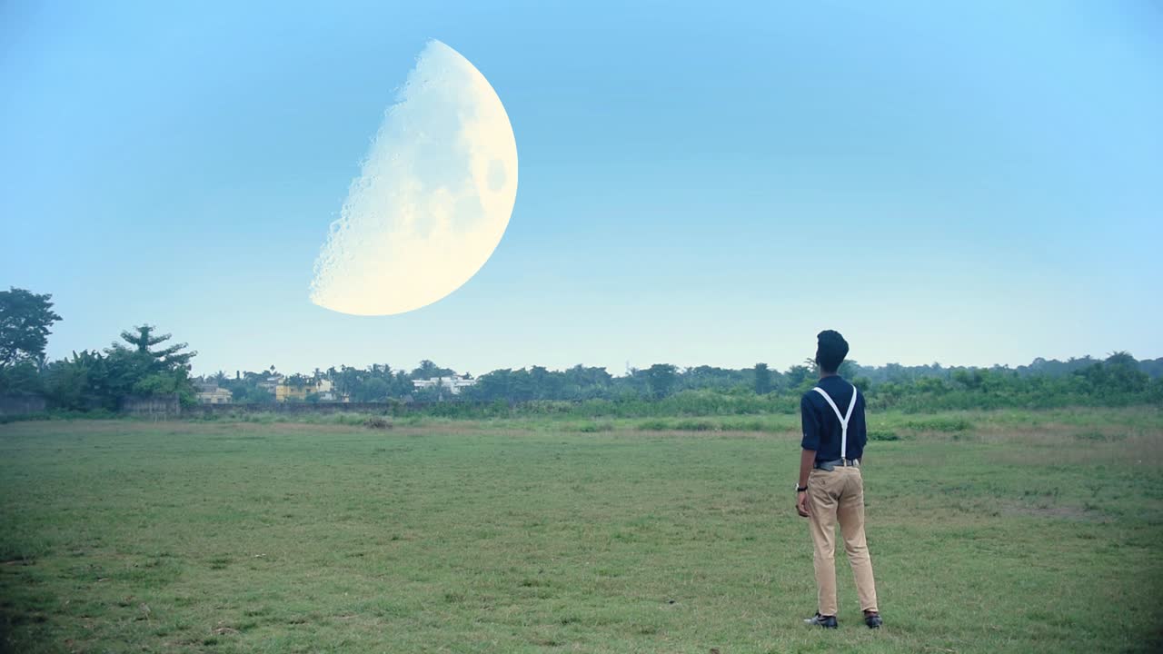 소년은 계곡이나 초원에 서서 꿈이나 공상과학에서 낮에 하늘에 있는 매우 큰 달을 바라보고 있습니다.