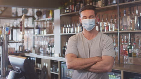 Portrait-Of-Male-Bar-Worker-Wearing-Face-Mask-During-Health-Pandemic-Standing-Behind-Counter