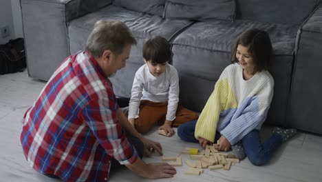 Glückliche-Kinder,-Die-Mit-Opa-Auf-Dem-Boden-Holzbauer-Spielen