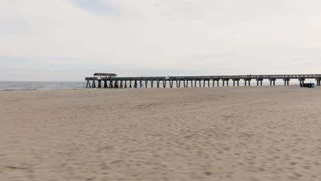 Drone-De-Una-Playa-Vacía-En-La-Isla-Tybee-Moviéndose-A-Través-De-La-Arena-Mirando-El-Muelle