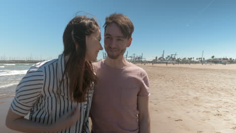 una pareja sonriente caminando por la playa en un día soleado