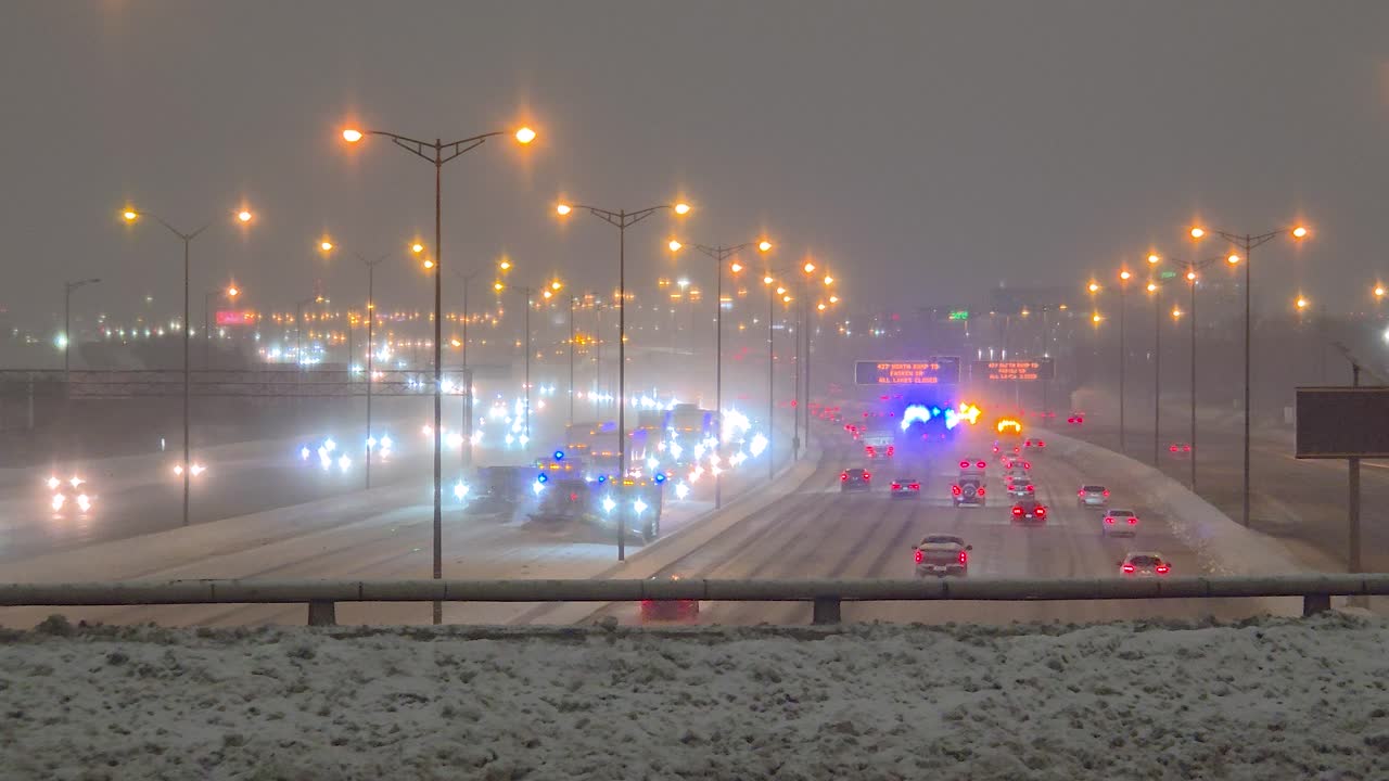 Snowplows clear highway at night with sirens, causing traffic jam