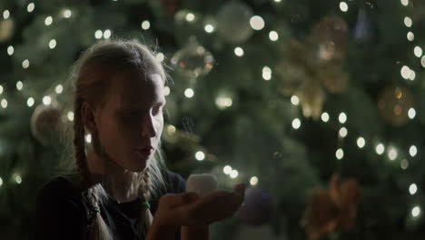 The-child-looks-at-the-burning-candle-in-his-hands.-Against-the-backdrop-of-blurry-Christmas-tree-lights.-Makes-a-wish