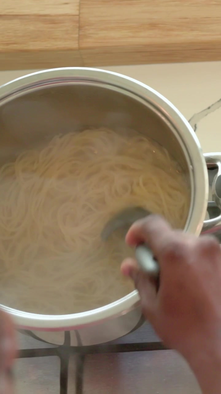 Video verticale: Mani che mescolano rompendo i pomodori in padella, mescolando la pasta per evitare che si attacchi ai fornelli.