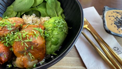 food bowl peanut sate sauce, brown rice, chicken, sweet potato, spinach, and avocado, in classy black bowl