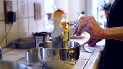 A-woman-chef-pouring-oil-from-a-measuring-cup-into-a-metal-mixing-bowl-while-baking-a-vegan-chocolate-cake-dessert-recipe