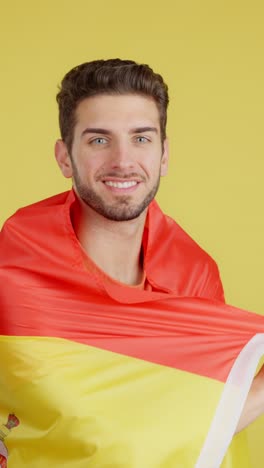 smiling young man with spanish flag draped over shoulders