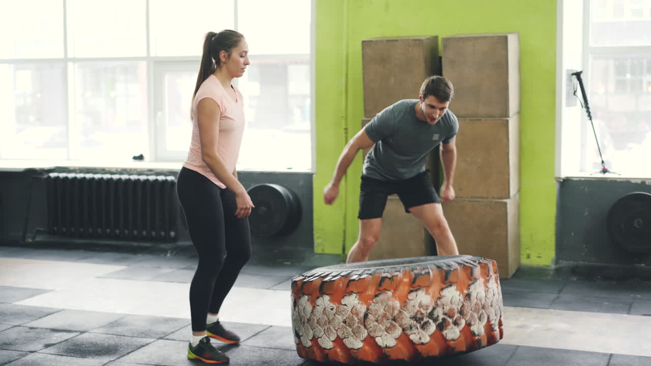 Woman and Man Lifting Tire in Gym