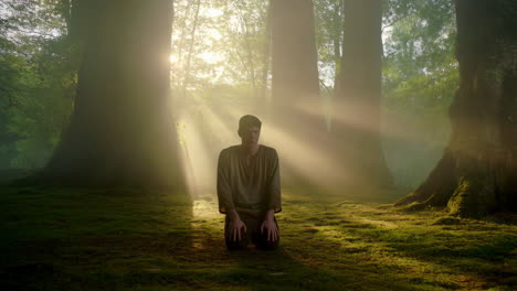 man kneeling in forest with light rays