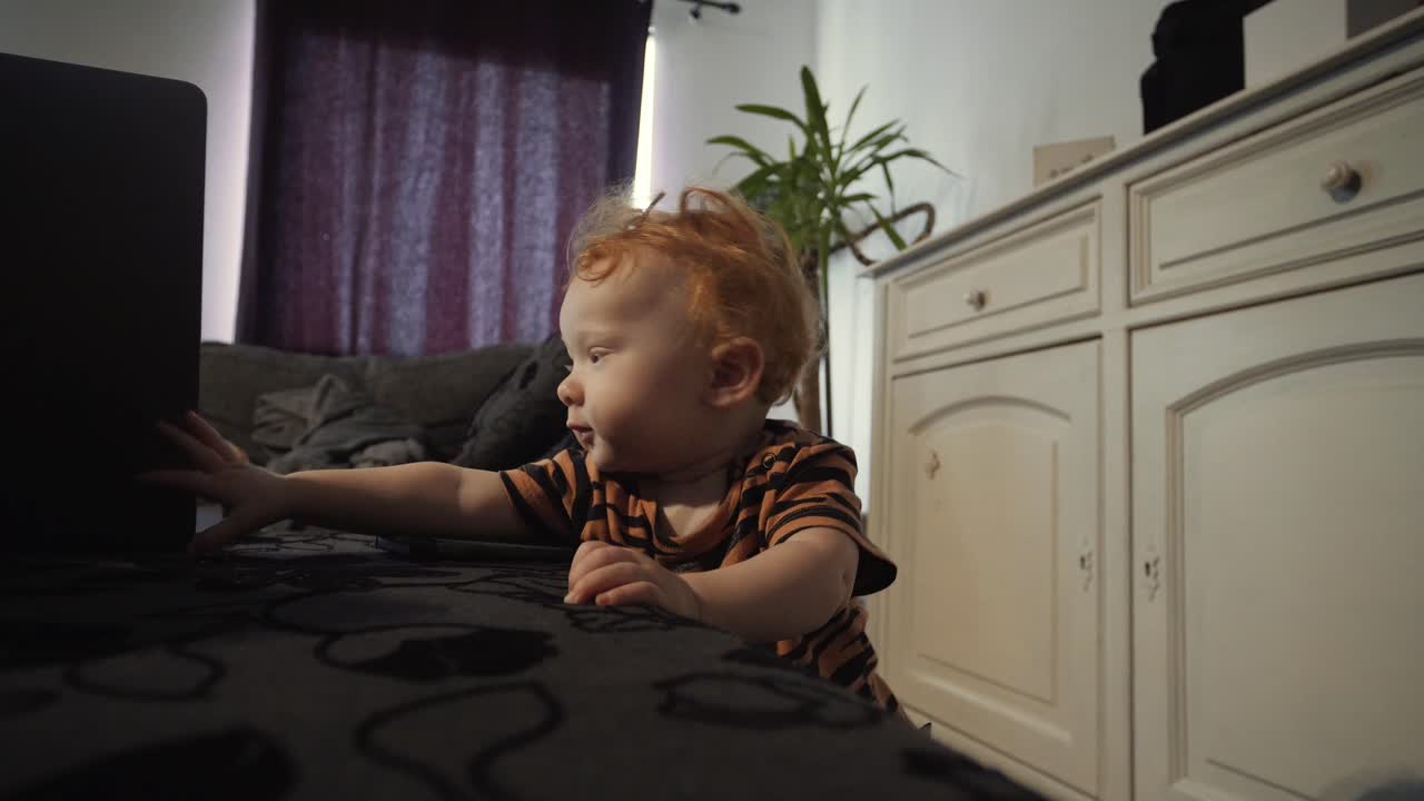 소파에 서있는 노트북을 얻으려고 노력하는 어린 소녀