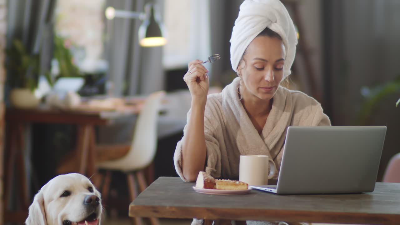 mujer trabajando desde casa con perro, comiendo pastel y bebiendo café