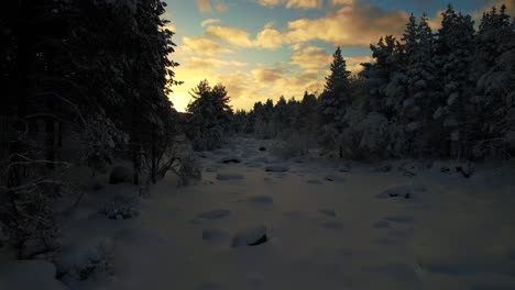 Drone-Vuela-A-Través-De-Un-Arroyo-Cubierto-De-Nieve-Al-Atardecer-En-Laponia,-Finlandia,-Círculo-Polar-ártico