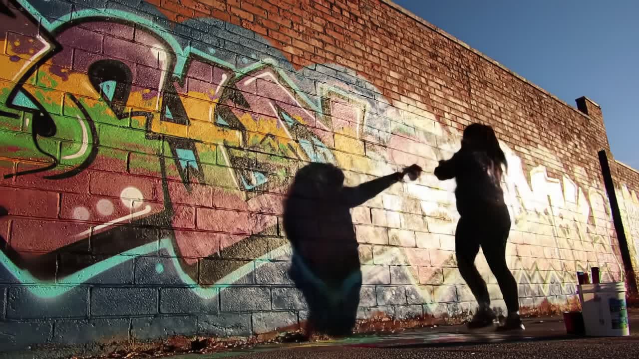 Vibrant Graffiti Art Creation: Artist Silhouetted Against Colorful Wall in Dynamic Street Art Scene Captured in Urban Setting at Dusk
