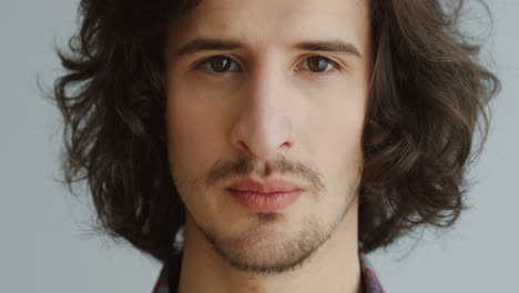 close up of the man's face with long hair looking straight in the camera and smiling on the white wall background