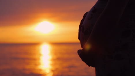 belly of a pregnant woman on a background of a beautiful sunset on the sea motherhood and expecting