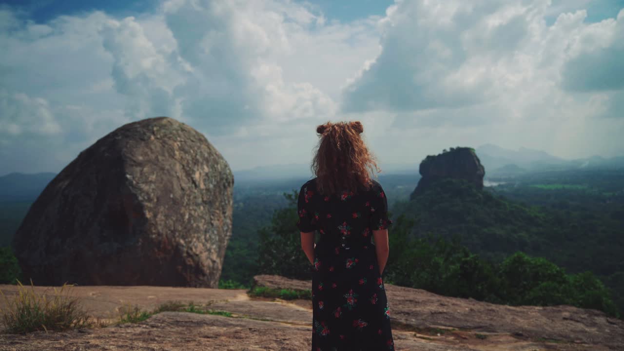 4K UHD Cinemagraph - seamless video loop of a young caucasian woman model at a viewpoint at the famous Sigiriya Rock in Sri Lanka next to an ancient buddhist temple in the rainforest