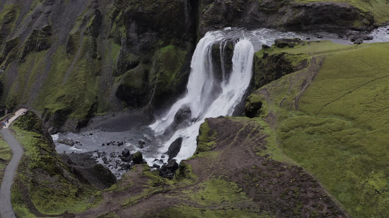 cascada fagrifoss que fluye en los acantilados volcánicos cubiertos de musgo con turistas mirando en la plataforma de observación en el sureste de islandia