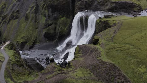 fagrifoss waterfall flowing at the mossy volcanic cliffs with tourists watching on the observation viewdeck in southeast iceland