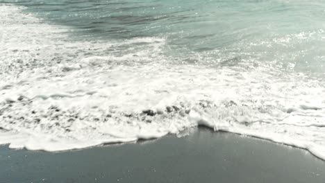 Person-barefoot-walking-on-black-sand-on-Tenerife-coastline,-POV