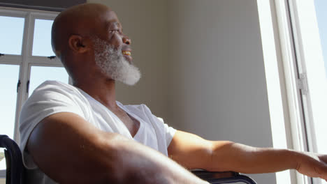 Low-angle-view-of-mature-black-handicap-man-sitting-on-wheelchair-near-the-window-at-home-4k