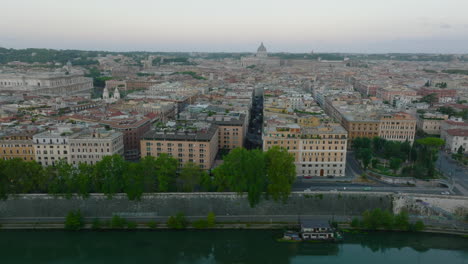 Sliding-reveal-of-apartment-buildings-on-Tiber-riverbank.-Aerial-view-of-urban-borough-and-basilica-in-Vatican-City-in-distance.-Rome,-Italy