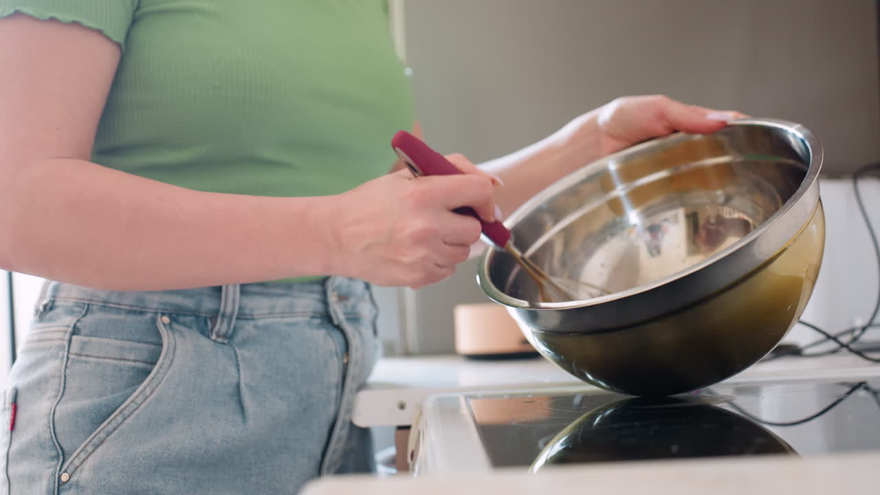 Close up side view of lady mixing egg with whisk in shiny stainless bowl on kitchen stove, preparing ingredients for baking homemade meal with focus on hands and casual cooking process