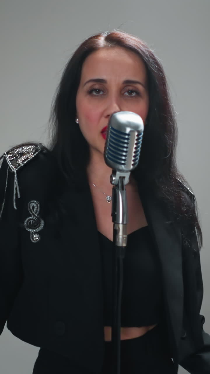 vocalista femenina en negro actuando en un micrófono vintage en un entorno de estudio minimalista, usando gestos de mano expresivos