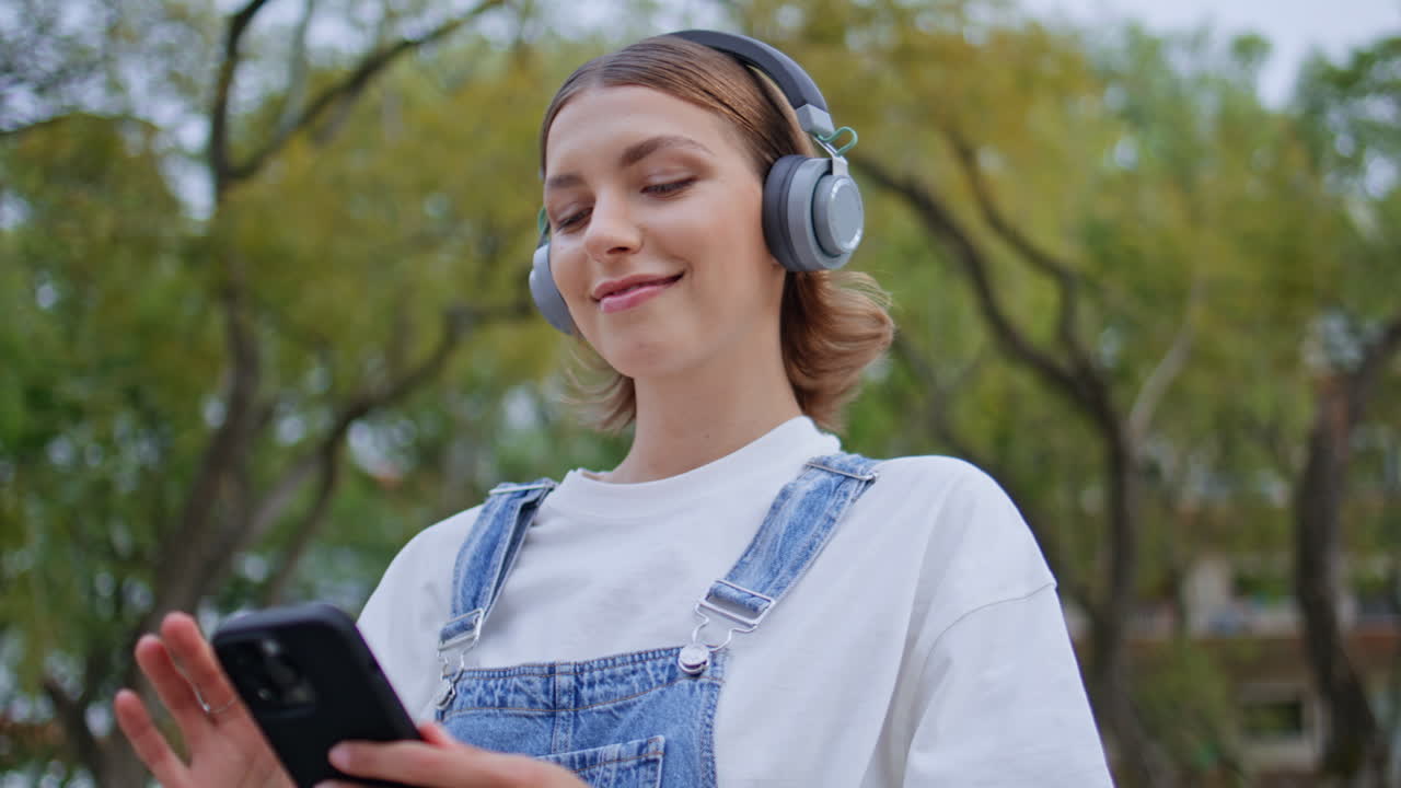 Happy girl enjoy song in headphones turning phone music app at street closeup