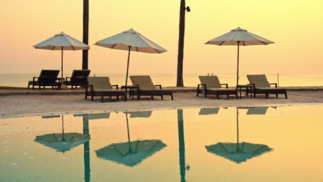 Strandliegen-Sitzen-Unter-Offenen-Sonnenschirmen-Vor-Einem-Rosa-Und-Gelben-Sonnenuntergang