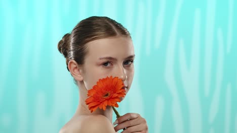 young woman holding gerbera flower with gentle smile a young woman with a gentle smile holds a vibrant orange gerbera flower against a serene blue background
