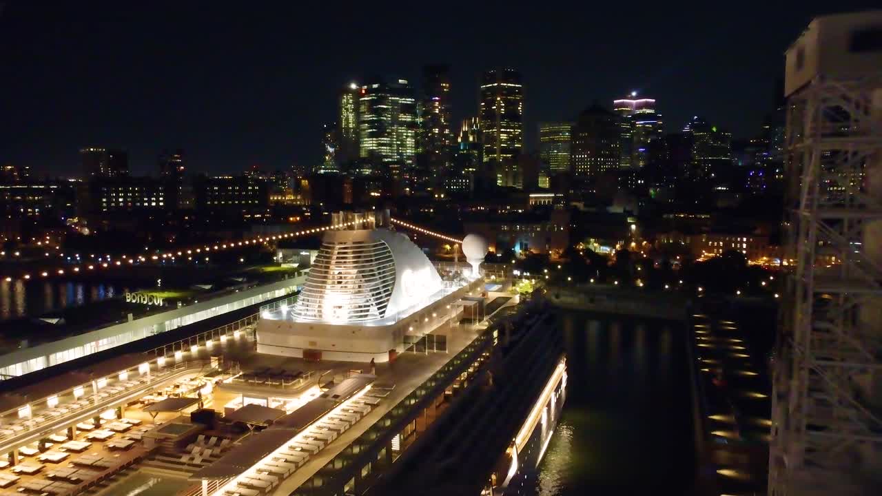 Aerial: Regent Seven Seas Grandeur cruise ship at night in Montreal harbor, Quebec, Canada, pull out drone shot