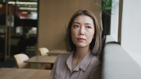 asian businesswoman sitting looking out of window in modern office