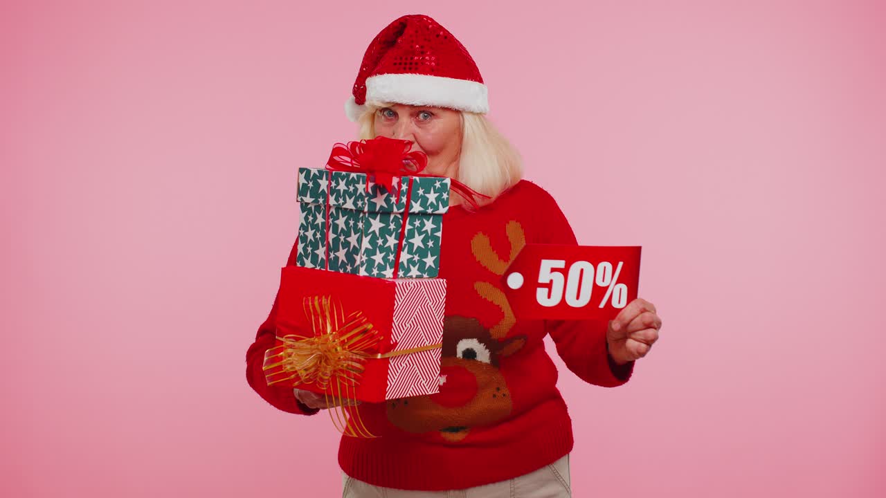 mujer anciana en suéter de navidad mostrando caja de regalos y 50 por ciento de descuento inscripciones texto de pancarta